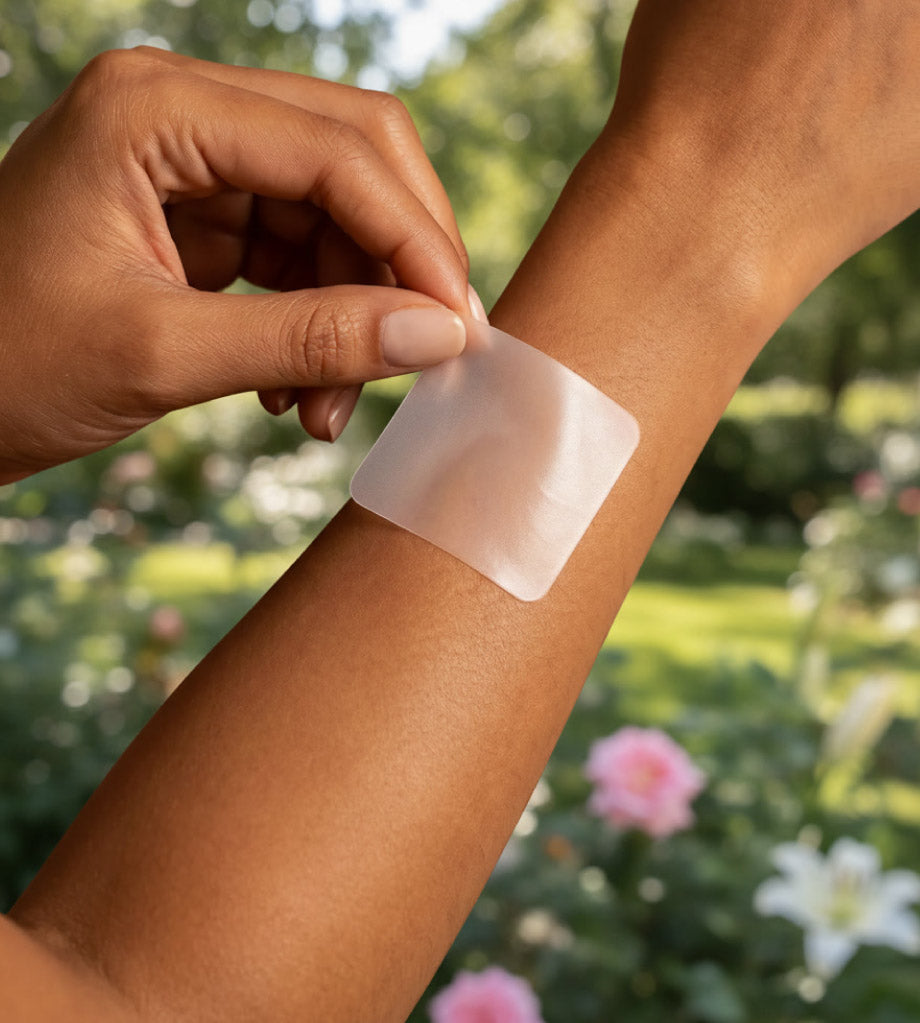Person applying a transparent adhesive patch to their arm with a garden background